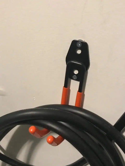 Keep Your EV Charging Cord Squared Away With This Rugged Wall Mount J Hook That Hangs Electric Vehicle Cables Up High To Dodge Rain And Dust For Stress Free Plugging Whenever You Need It; black and orange j hook mounted on wall with EV charging cord.