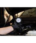 Engine compression test gauge held by gloved hand under car hood; 2-3/4 in Bourdon dial