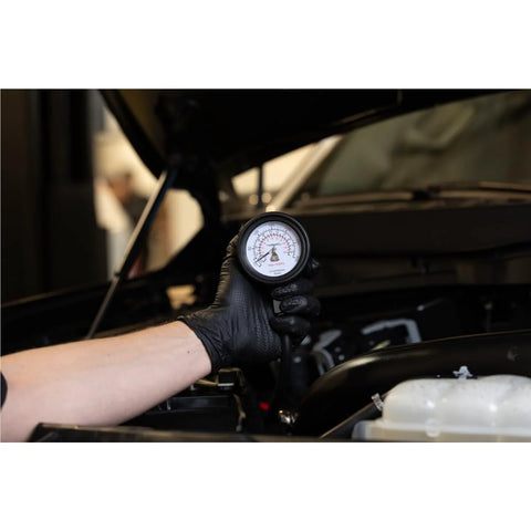 Engine compression test gauge held by gloved hand under car hood; 2-3/4 in Bourdon dial