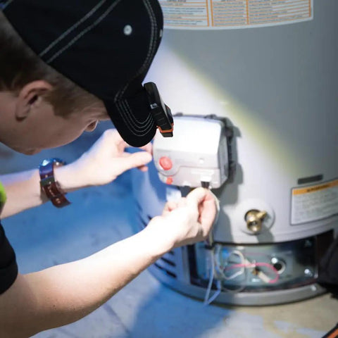 Person wearing Cap Visor Clip LED Light With Pivoting Head, Battery-Powered 2xAAA, working on appliance.