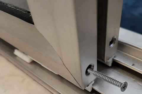 Close-up of Badass Stainless Steel Self Threading Screw inserted into framed shower door panel, securing aluminum track.