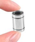 LM8UU linear ball bearing, silver metal cylinder with inner bore and rubber seals, held between fingers