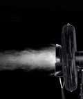 Heavy Duty Oscillating Mist Fan With Three Speed Levels And Adjustable Pedestal spraying fine mist in a dark setting.