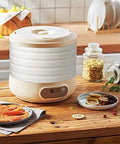 Electric Fruit Dehydrator featuring five sturdy trays on a kitchen counter with dried fruits, herbs, and jars.