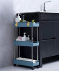 Navy blue Three Tier Slim Mobile Shelving Unit On Wheels With Slide Out Storage Cart beside a bathroom vanity.