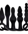 Five black silicone plugs from Super Cool Five Piece Silicone Butt Plug Training Kit For Beginners with tapered design and retrieval rings.