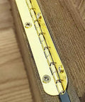 Close-up of a golden metal hinge installed on a wooden surface for Two Pack Golden Metal Hinges For Cabinets And Furniture Hardware Long Gold Hinges For Jewelry Boxes And Wooden Cases Antique Vintage Look Slick For Farmhouse Decor And DIY Furniture Repair Projects.