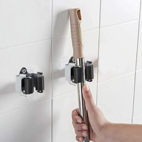 Hand placing a broom into Heavy Duty Wall Mounted Mop Broom Holder Rack Set Of 10 Clips That Grips Like A Pro on white tile wall.