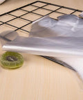 Disposable transparent plastic food prep gloves, unrolled sheet on a wooden table beside a metal wire rack
