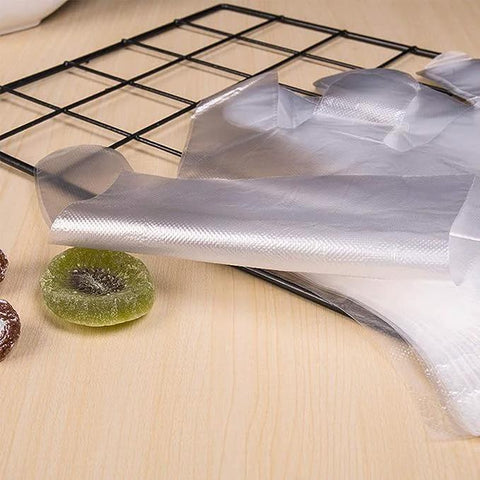 Disposable transparent plastic food prep gloves, unrolled sheet on a wooden table beside a metal wire rack