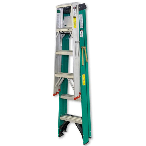 A green and silver folding ladder standing vertically, against a white background, with safety labels visible.