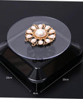 Solar Powered Rotating Jewelry Display Stand With Built In Kickstand showcasing a pearl brooch on a sleek ABS turntable.