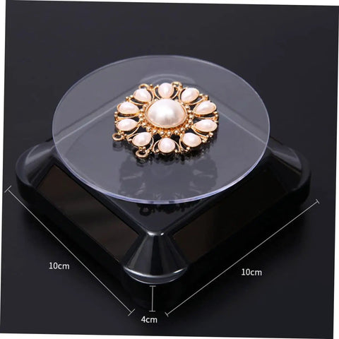 Solar Powered Rotating Jewelry Display Stand With Built In Kickstand showcasing a pearl brooch on a sleek ABS turntable.