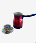 Red Electric Turkish Coffee Pot Kettle With Cool Touch Handle And Stainless Steel Body Travel Size 0.3L Fast Boil In Minutes next to a cup