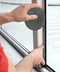 Grey Bruiefpap self-adhesive weather-stripping roll installed on a window frame for door insulation.