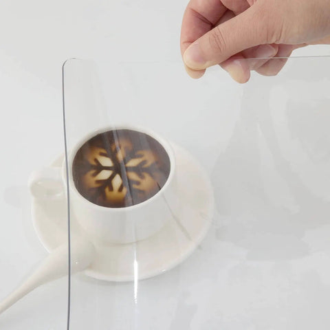 Hand holding Clear 24 By 60 Inch Table Protector 1.5mm Thick PVC Desk Mat Kid Friendly Waterproof And Easy To Clean with cup underneath
