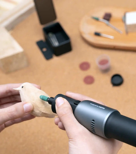 Person using Badass Sixty Piece Rotary Tool Accessory Crate for detailed carving of a wooden bird figurine.