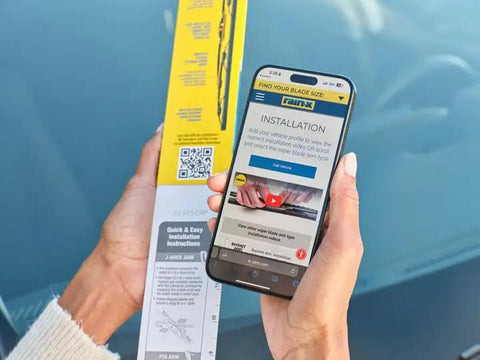 Person using phone for WeatherBeater Wiper Blades 26 Inch And 18 Inch Two Pack installation guide next to car windshield
