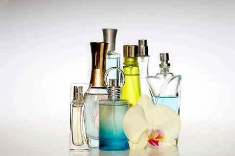 Assorted colorful perfume bottles with a white orchid flower on a light background.
