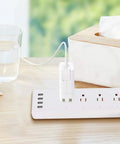 Totally Smooth Smart Power Strip With Four Wall Outlets And Four USB Charging Ports on a wooden table with a glass of water.