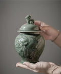 Top Tier Ceramic Airtight Tea Canisters For Loose Tea Leaves And Coffee Beans Hand Embossed Celadon Kirin Design held by a hand.