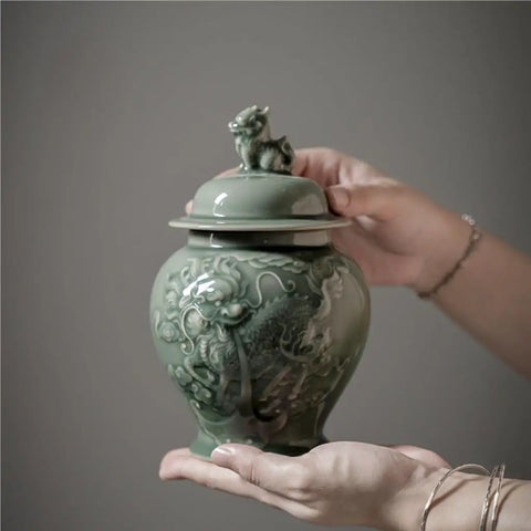 Top Tier Ceramic Airtight Tea Canisters For Loose Tea Leaves And Coffee Beans Hand Embossed Celadon Kirin Design held by a hand.