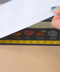 Hand lifting a sheet revealing colorful graphics on Top Shelf Chalkboard Style K-2 Desk Reference Mats, Built Tough Premium Plastic Teaching Companions For Elementary Students, Teacher Go To Back To School Classroom Supplies, 24 Pack Hassle Free Multi Grid Learning Boards.