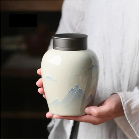 Top Shelf Ceramic Tea Storage Jar With Hella Secure Lid For Loose Leaf And Daily Coffee Beans Vintage Kitchen Caddy held in hand with mountain design.