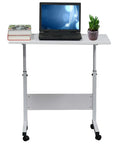 Adjustable standing computer desk with steel frame, white top, laptop, books, and plant for cozy living room setups.