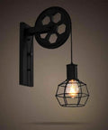 Straight Up Industrial Black Metal Cage Wall Sconce Featuring Heavy Duty Steel Frame Adjustable Pulley Pull Chain Clear Glass Cylinder E26 Socket Vintage Loft Wall Light For Kitchen Dining Room Cafe mounted on wall with visible pulley mechanism.