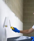 Person applying Super Slick Basement Sealer White 5 Gallon to concrete wall with a roller for a smooth finish.