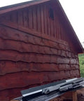 Top Shelf One Coat Wood Stain And Sealer For Thermally Modified Exterior Decking In Bold Black Canyon Red Semi Transparent Color With Hella Durable UV And Mildew Protection Knockout Natural Grain Enhancement applied on a wooden wall.