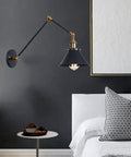 Heavy Duty Industrial Swing Arm Wall Sconce Built Tough For Living Spaces Vintage Metal Light Fixture, black and brass design above a bed.