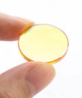 CO2 laser focal lens, 20mm diameter, orange-tinted glass held between fingers