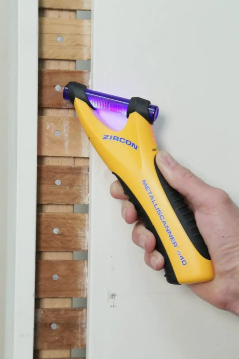 Hand using MetalliScanner M40 Handheld Electronic Metal Detector For Drywall Concrete Lathe And Plaster Stucco.