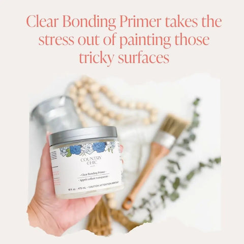 Close-up of a hand holding a 32 oz quart of Clear Bonding Primer for Chalk Style Furniture Prep with a brush and decor in background.