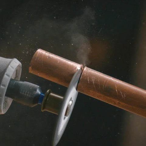 Close-up of a rotary tool with an EZ Lock cutting wheel cutting a copper pipe.