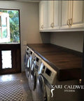 Laundry room with three washing machines, a wooden countertop, and white cabinets against a gray wall.