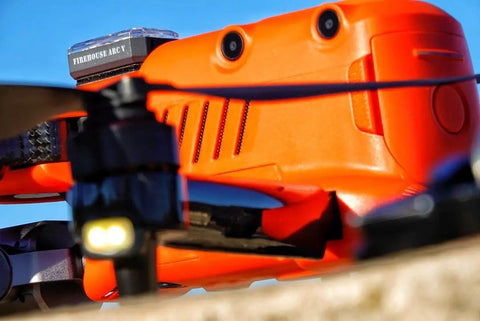 Close-up of an orange drone with an Arc V Pro Grade Multi Color Drone Strobe With Remote Control attached on top.