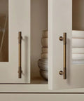 Close-up of 6 pack antique brass kitchen cabinet pulls with 5 inch center to center spacing on cream cupboard doors