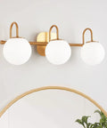 Three Light Vanity Light Fixture For Bathroom With Brushed Brass Frame And Milk White Glass Globes Over Mirror