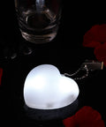 Heart-shaped purse light with sensor, glowing white, surrounded by red petals. Battery-powered night light for handbags.