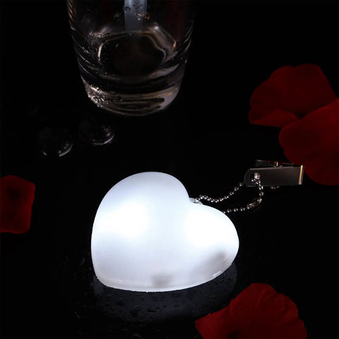 Heart-shaped purse light with sensor, glowing white, surrounded by red petals. Battery-powered night light for handbags.
