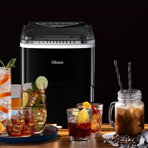 Front view of Silonn countertop ice maker with black body and transparent lid, surrounded by drinks.