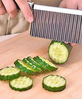 Kitchen vegetable slicer with steel wavy blade slicing cucumber rounds on a cutting board