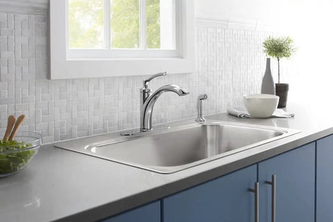 Modern kitchen with stainless steel sink, faucet, and gray countertop, view showing sink area under window with natural light.
