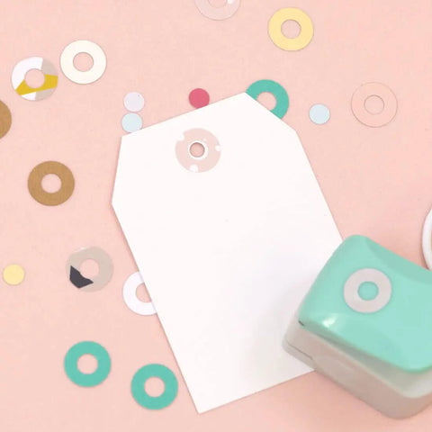 Circle Punch With Reinforcing Ring And Snap Lever For Paper Crafting on pink background with punched grommets and white tag.