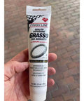 Heavy Duty Built Tough Bike Grease With High Pressure And Water Resistant Formula For Rust And Corrosion Protection Of Headsets Hubs And Bottom Brackets 3.5 Oz Ideal For Mountain And Road Bikes in a tube held by a hand on a red brick background