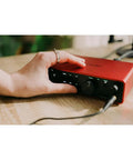 Person adjusting Scarlett 2i2 4th Gen Audio Interface Bundle With OnStage MC20 20ft XLR To XLR Mic Cable on wood desk.