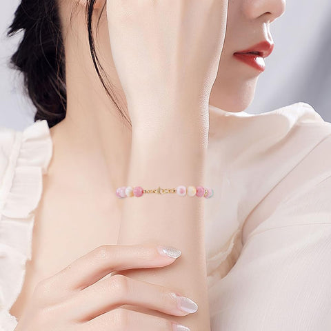Pink and white beaded bracelet on woman's wrist with gold clasp, highlighting jewelry detail.